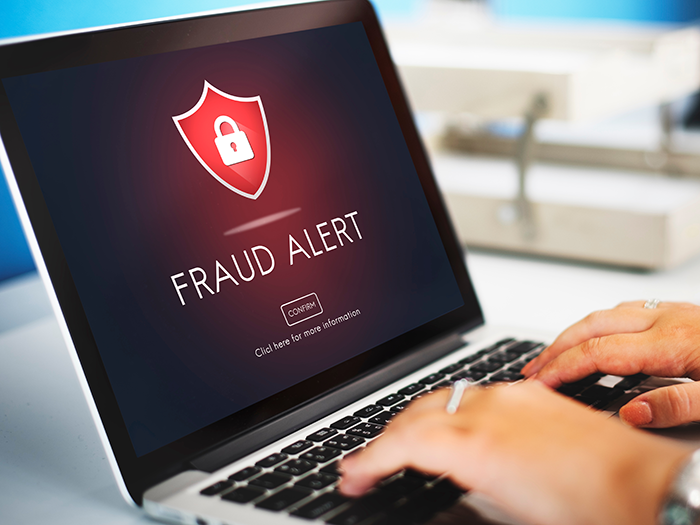 Person's hands typing on laptop screen with Fraud Alert and lock symbol on screen