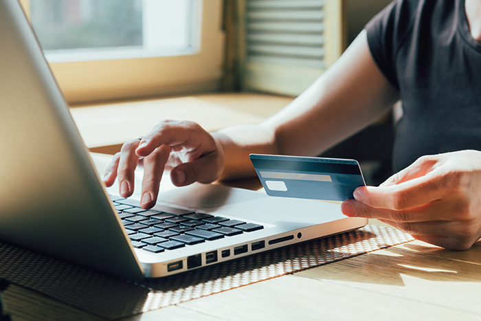Person's hands typing on laptop while holding a credit card