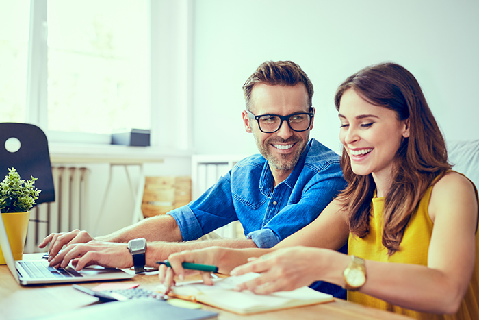 Man smiling at woman while typing on laptop and woman is smiling and writing on journal
