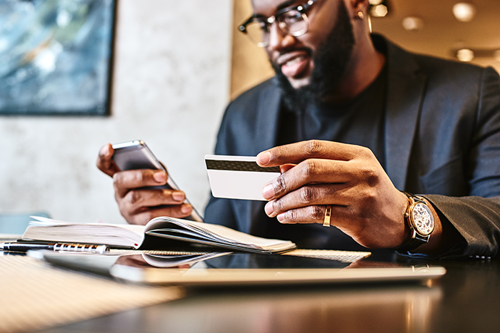 Man smiling and holding a credit card while looking at a smartphone