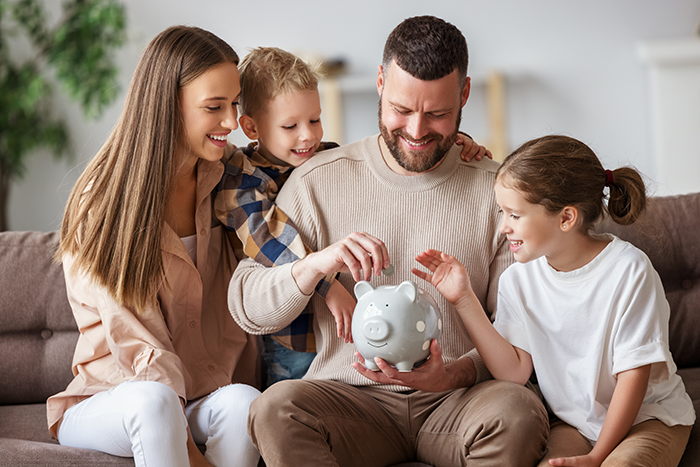 Woman and man smiling and showing two kids how to put money into piggy bank
