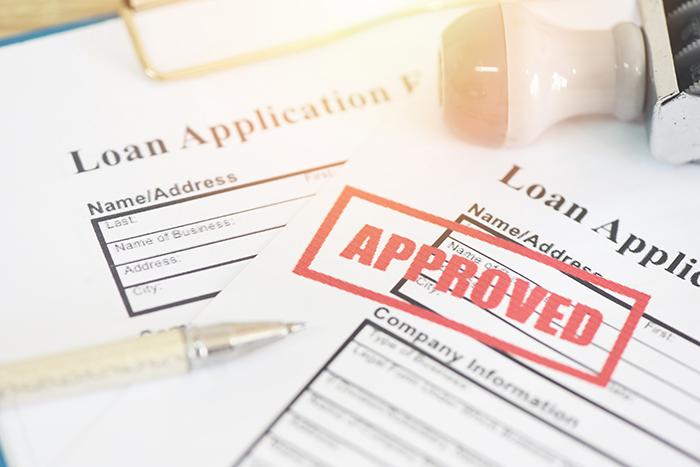 Paper loan applications with red Approved stamp and pen