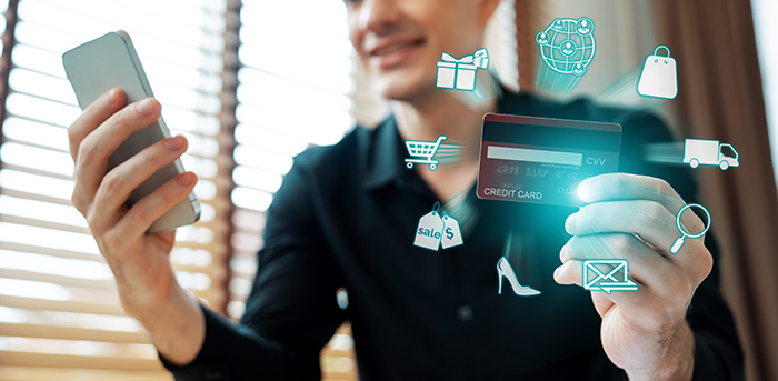 Man holding phone in one hand and credit card with shopping icons hovering above it